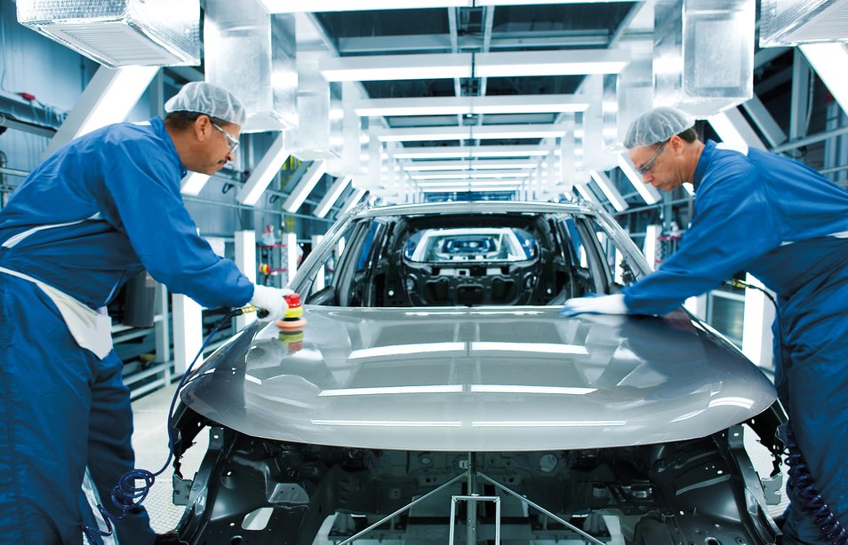 Two workers stand beside a vehicle in a production center