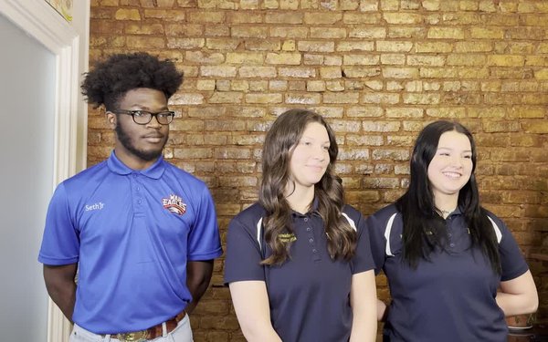 Three high school students stand against a brick wall being filmed for a video interview