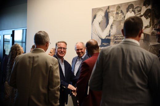 Two men shaking hands and smiling in a crowd of people at the Good News Gathering