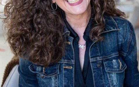 Edie headshot wearing a denim jacket and smiling at camera with long dark wavy hair