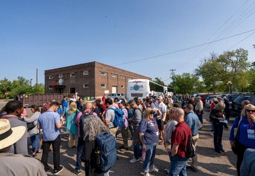 Group of people stand outside on a tour with a bus and brick building the background