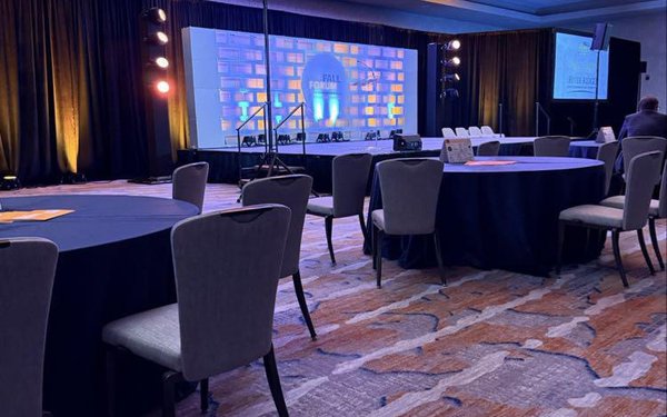 Site selection guild fall forum stage in an auditorium with spotlights, chairs, and tables